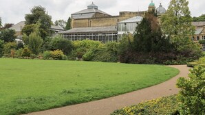A large green lawn with a paved path leading to a building with a glass conservatory. - 2B Cavendish Villas (Buxton)