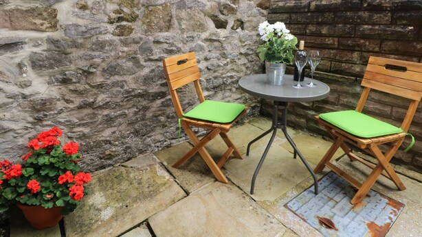 A stone wall with a metal table and two wooden chairs with green cushions. - 2B Cavendish Villas (Buxton)