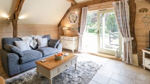A cozy room with a wooden ceiling, a blue sofa, a wooden coffee table, and a large window with curtains. - The Barn at Rapps Cottage (Ilminster)