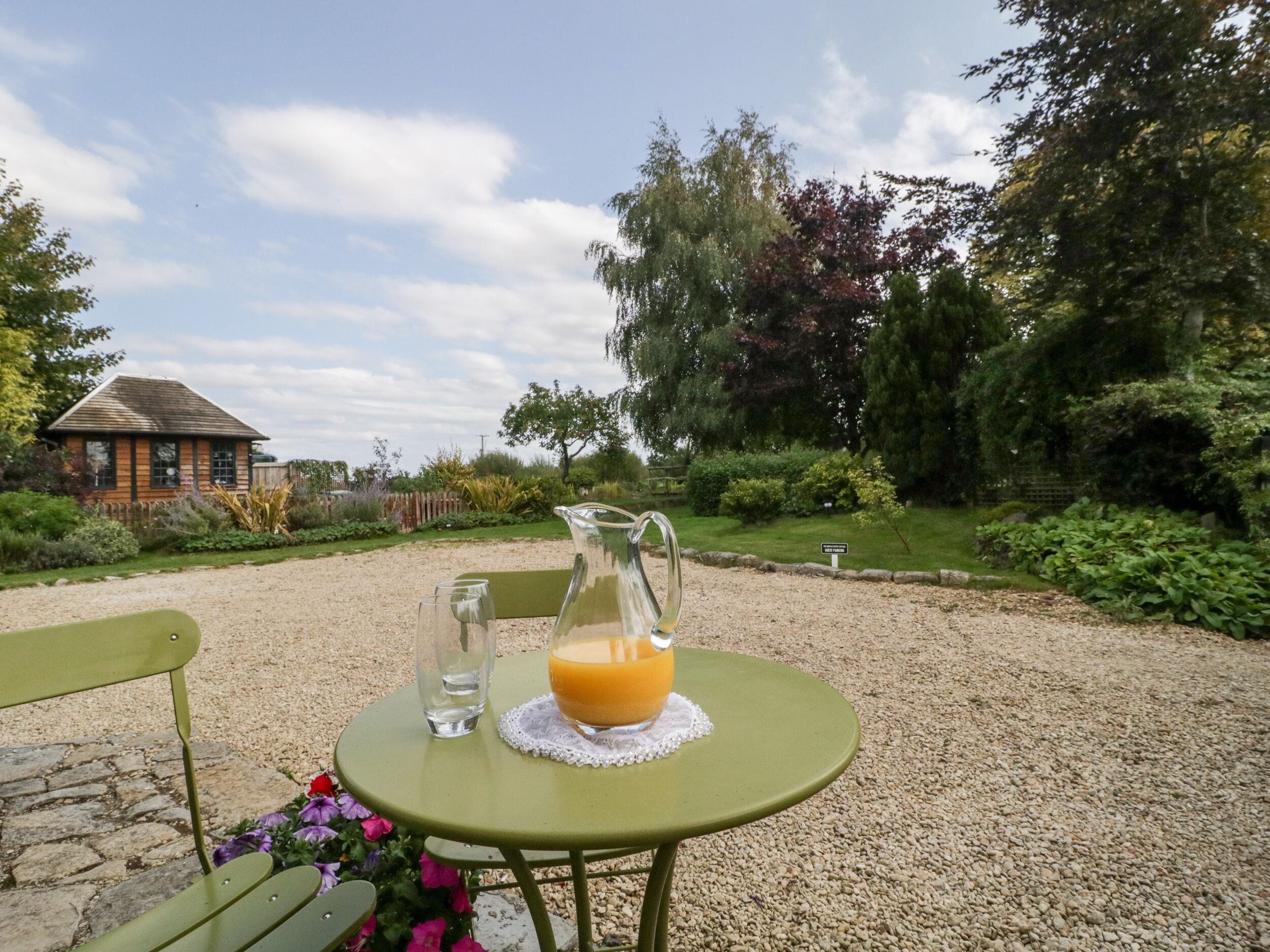A table with a pitcher of orange juice, a glass of water, and a glass of orange juice on a gravel surface.