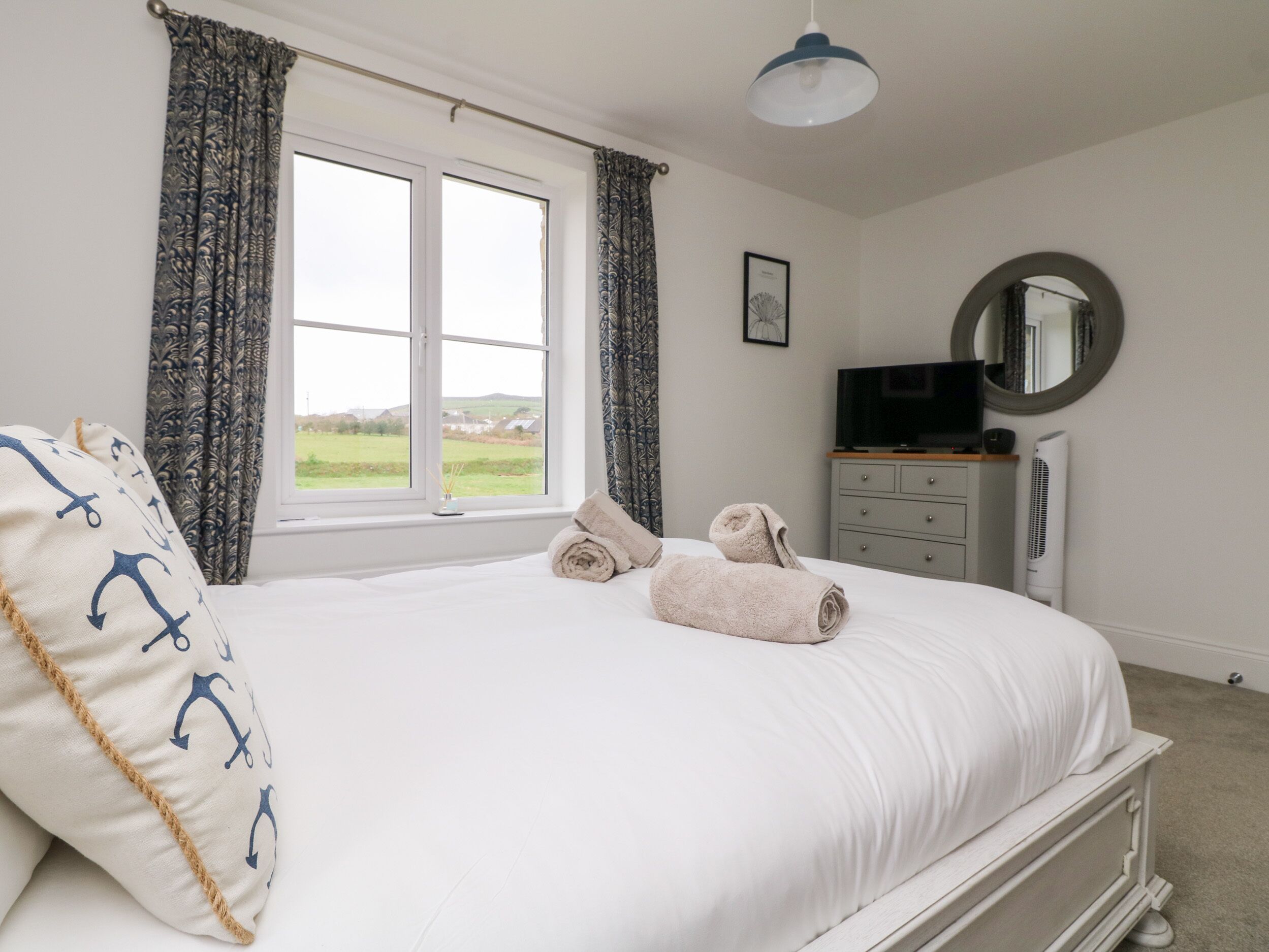 A bedroom with a large bed, a TV, a dresser, and a window with curtains.