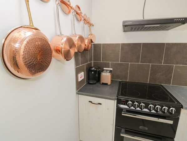 A kitchen with a black stove, a coffee maker, and a toaster on the counter. - Llawenfan (Criccieth)