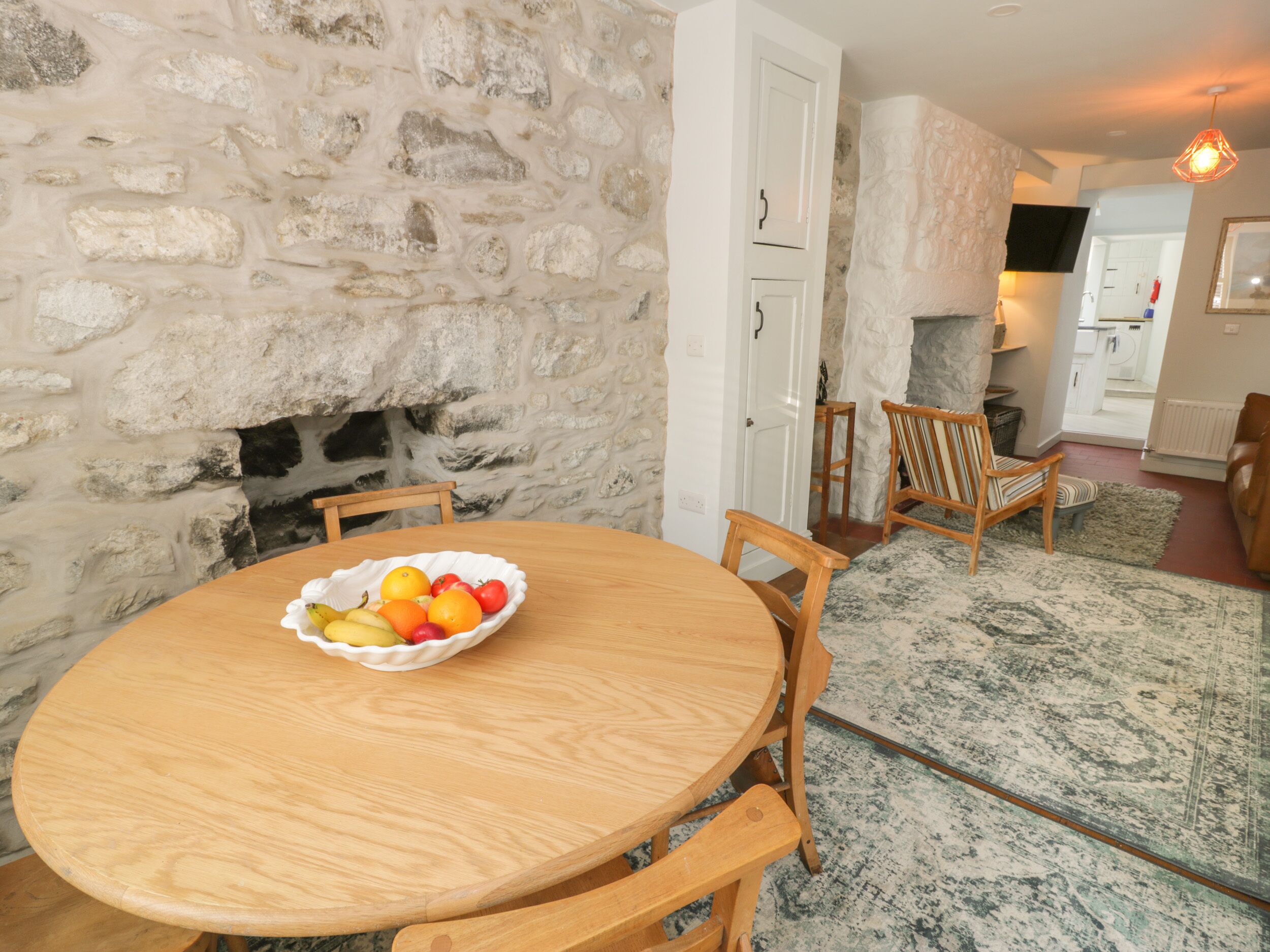 A stone wall, wooden dining table with fruit, and a cozy living area with a fireplace.