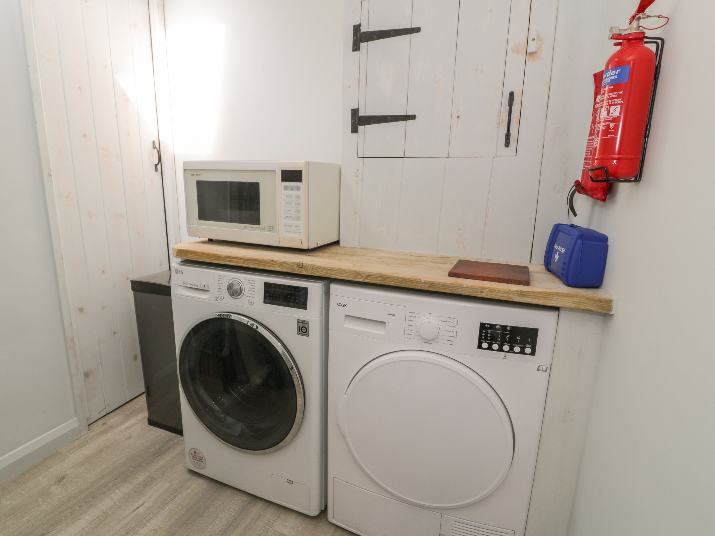 A laundry area with a washing machine, dryer, microwave, and a fire extinguisher.