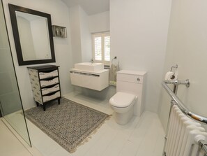 A modern bathroom with a white sink, toilet, and a large mirror. There is a patterned rug on the floor and a radiator on the right. - Llawenfan (Criccieth)