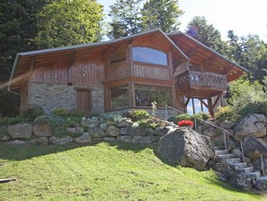 A two-story wooden house with a stone foundation, a balcony, and a stone staircase leading to the entrance.