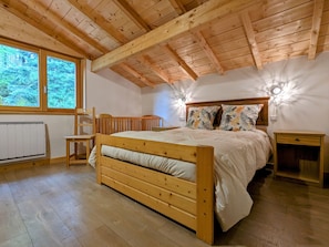 Une chambre à coucher avec un cadre en bois, comprenant un lit, une chaise, une table de chevet et une fenêtre donnant sur des arbres.