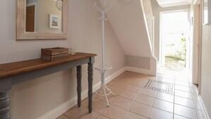 A hallway with a wooden console table, a coat rack, a mirror, and a tiled floor. - 4 Fishermans Wharf (Whitstable)
