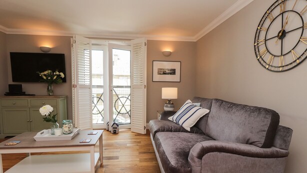 A living room with a grey sofa, a coffee table, a TV, and a large wall clock. - 4 Fishermans Wharf (Whitstable)