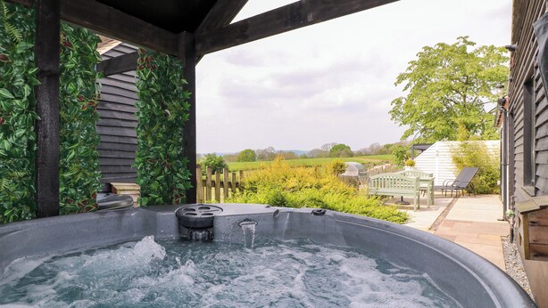 A hot tub with a view of a garden and a wooden deck. - The Coach House, Bank Top Farm (Ashbourne)