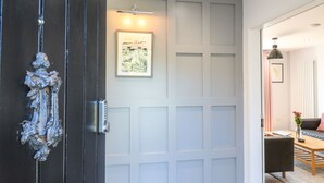 A modern interior with a dark wooden door, a white paneled wall, and a framed artwork above it. - The Coach House, Bank Top Farm (Ashbourne)