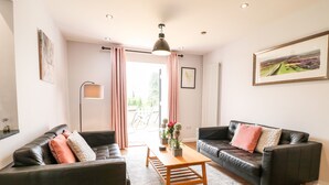 A modern living room with two black leather sofas, a wooden coffee table, and a large window with curtains. - The Coach House, Bank Top Farm (Ashbourne)