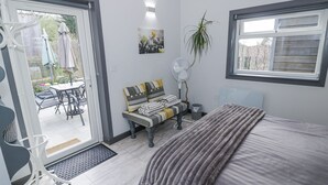 A bedroom with a bed, a bedside table, a chair, a fan, a window, and a door leading to a patio area with outdoor furniture. - The Garden House (Stratford-upon-Avon)