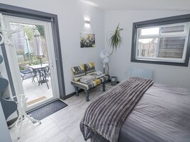 A bedroom with a bed, a bedside table, a chair, a fan, a window, and a door leading to a patio area with outdoor furniture.