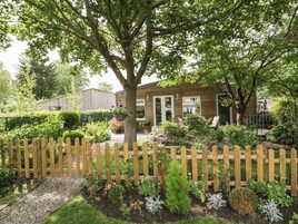 A wooden house with a garden in front, a wooden fence, and a gravel path.
