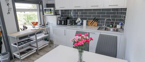 A compact kitchen with white cabinets, a black tiled backsplash, a coffee maker, and a vase of pink flowers on the counter.