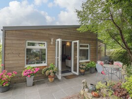 A wooden cabin with a patio, a dining area, and a garden with potted plants and a statue.