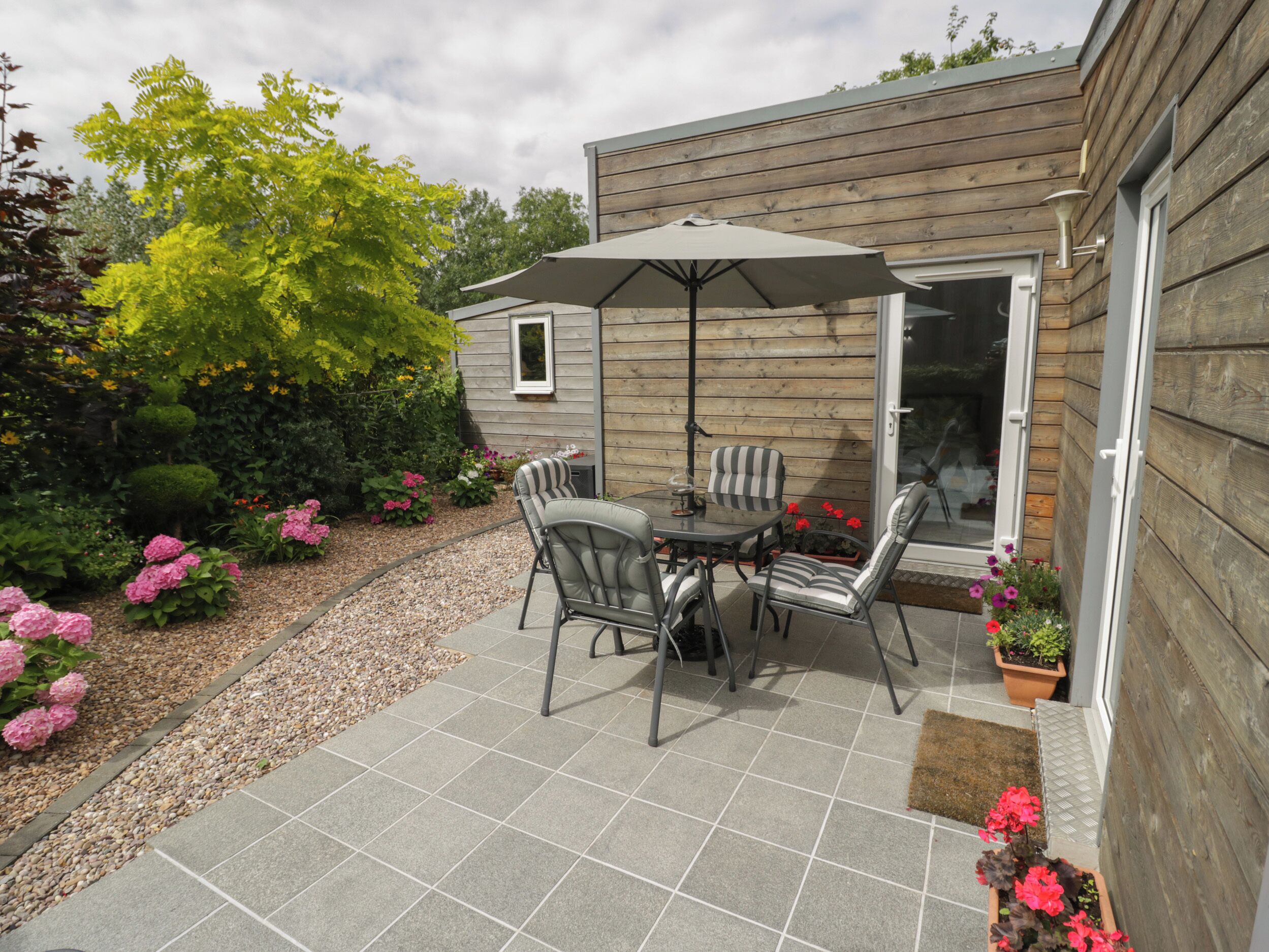 A patio with a table and chairs, surrounded by a garden with various plants and flowers.