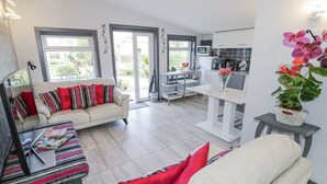 A modern living room with a sofa, a coffee table, and a dining area with a table and chairs. There is a kitchen with white cabinets and a microwave. - The Garden House (Stratford-upon-Avon)