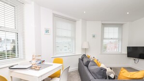 A modern living room with a grey sofa, yellow chairs, a white desk, and a flat-screen TV mounted on the wall. - Beach Rose (Teignmouth)