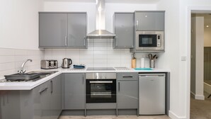 A modern kitchen with grey cabinets, a stainless steel microwave, a built-in oven, and a dishwasher. - Beach Rose (Teignmouth)