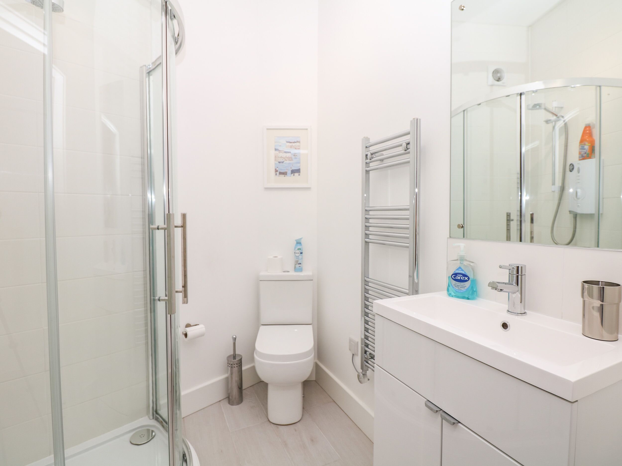 A modern bathroom with a glass shower enclosure, a white toilet, a sink with a mirror, and a towel rack.