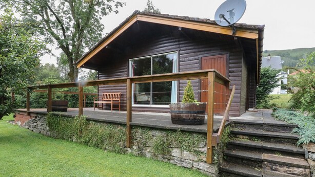 Une cabane en rondins avec une véranda, un banc et une antenne parabolique.