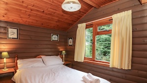 Une chambre à coucher dans un chalet en bois, avec un lit, deux lampes de chevet, une fenêtre avec des rideaux et des tableaux encadrés accrochés au mur.