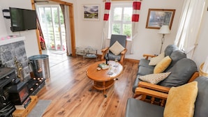 A cozy living room with a fireplace, a sofa set, a coffee table, and a television mounted on the wall. - Lough Mask Road Fishing Cottage (Neale)