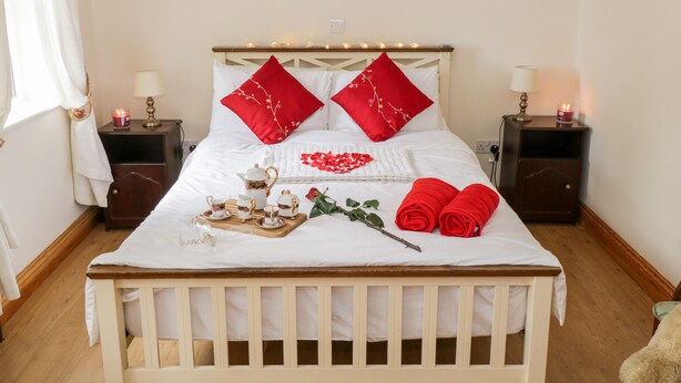 A neatly made bed with red pillows, a bedside table with a lamp, and a tray with tea sets. - Lough Mask Road Fishing Cottage (Neale)