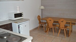 A compact kitchen with a microwave, a small refrigerator, a stove, and a dining table with four wooden chairs. - T3 Apartment at the foot of the slopes with covered parking (Les Angles)