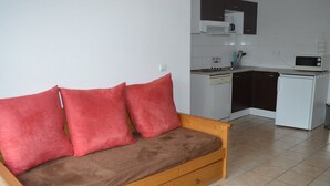 A small living area with a wooden sofa, a wooden coffee table, and a kitchenette in the background. - T3 Apartment at the foot of the slopes with covered parking (Les Angles)