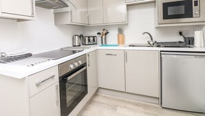 Een moderne keuken met witte kasten, een oven van roestvrij staal, een magnetron en een vaatwasser.