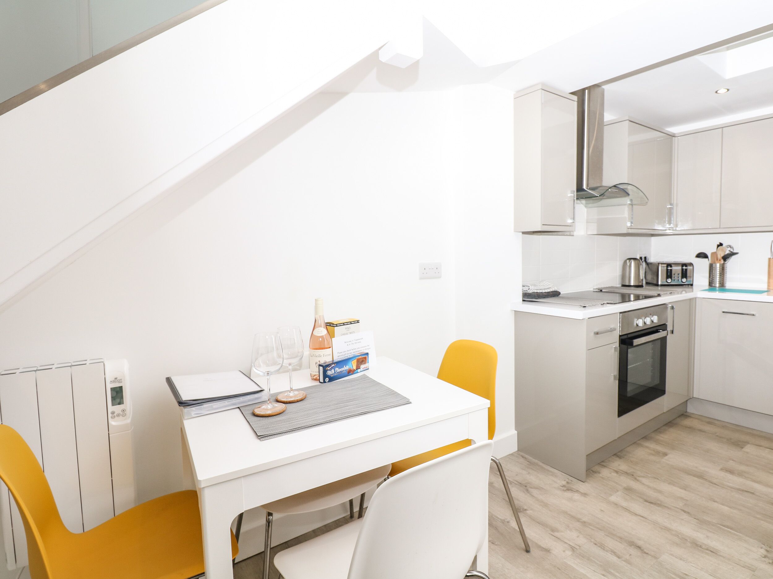 A modern kitchen with white cabinets, a built-in oven, and a dining area with a white table and yellow chairs.
