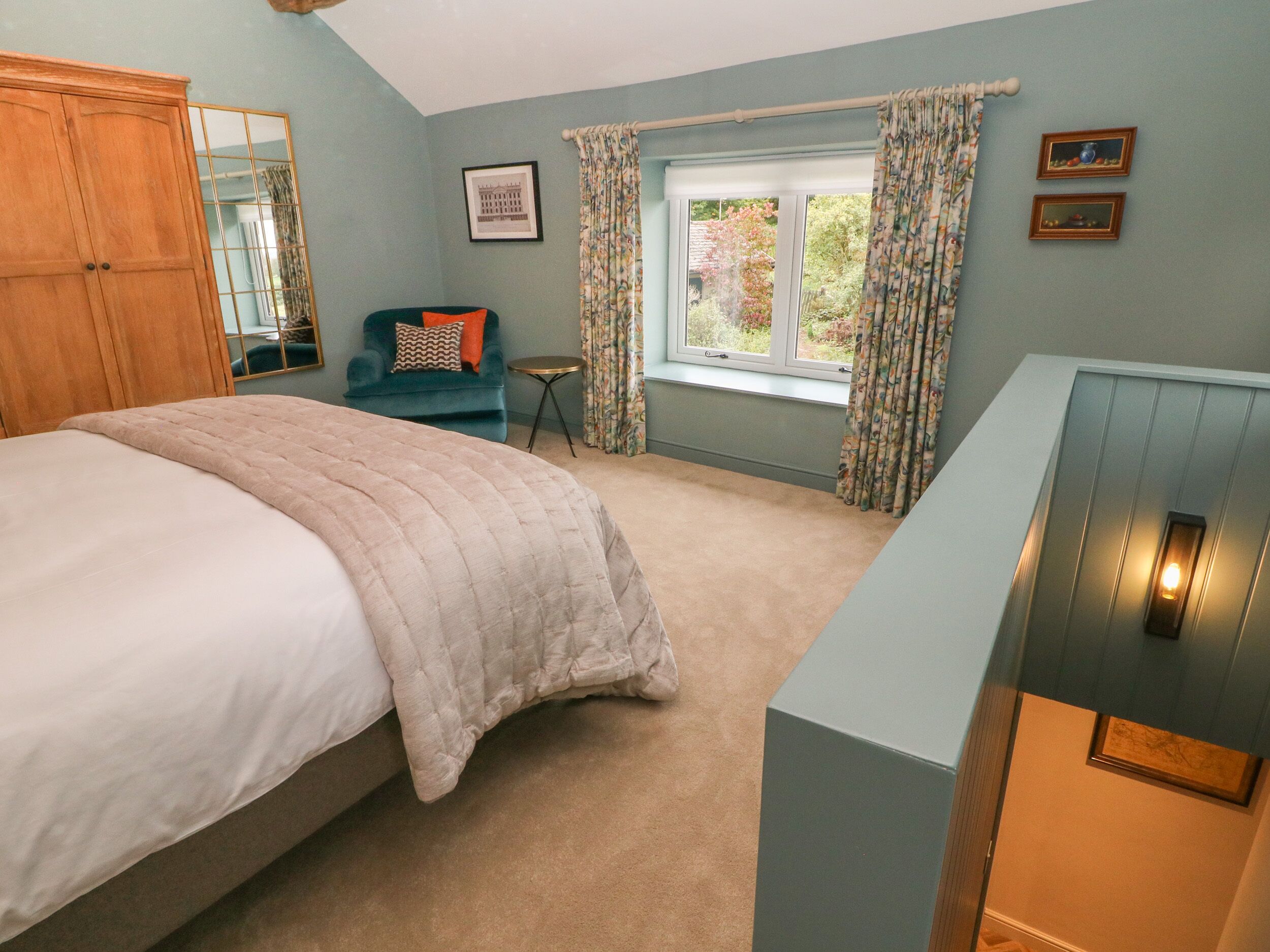 A bedroom with a bed, a blue dresser, a chair, a small table, and a window with curtains.