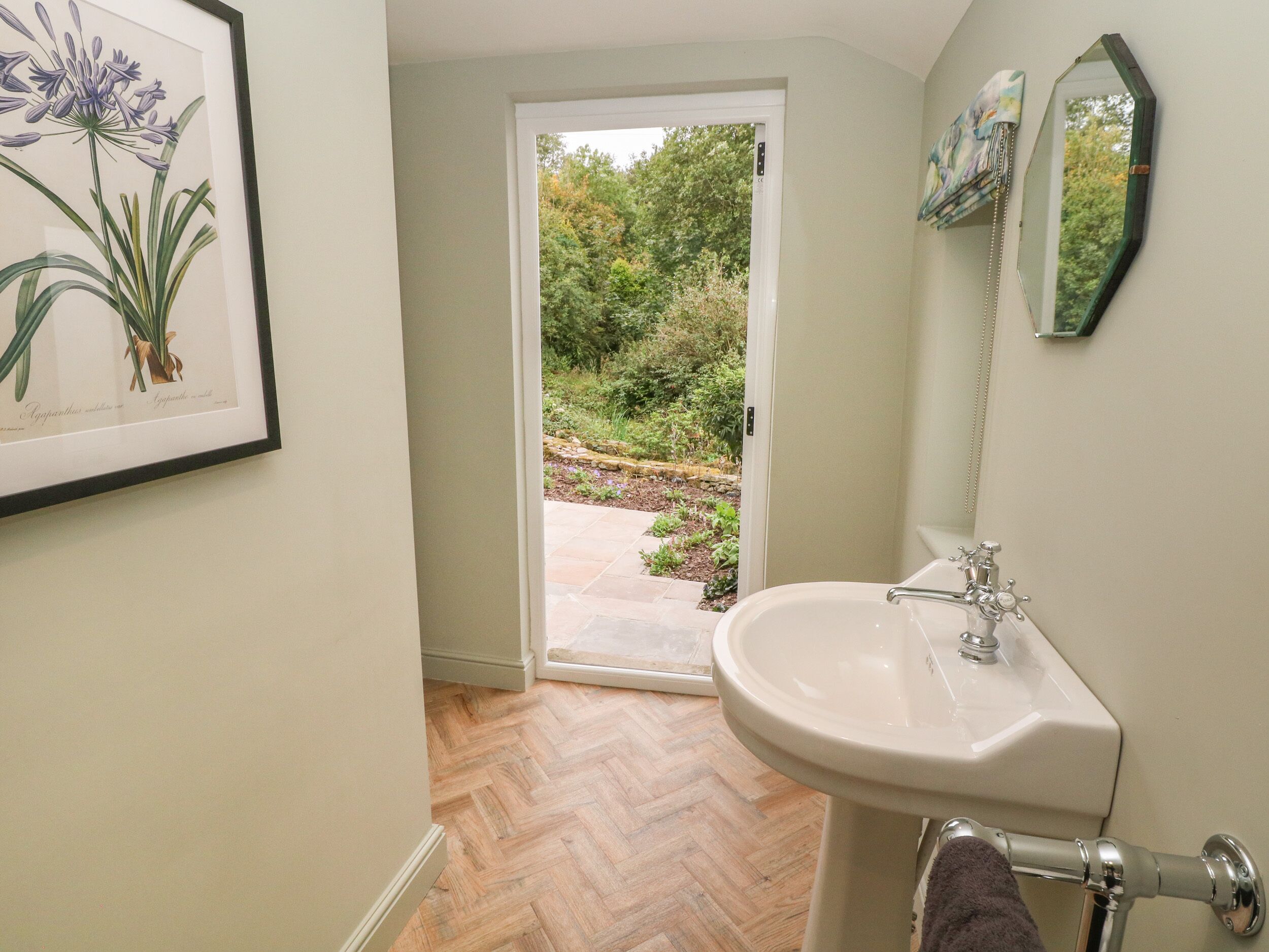 A bathroom with a white sink, a mirror, and a door leading to a garden.