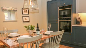 Un coin repas avec une table en bois mise pour deux personnes, deux chaises, une bouteille de vin et un vase avec une plante.