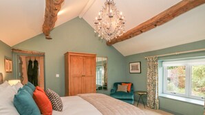 Une chambre avec un grand lit, une armoire en bois, un lustre, une chaise et une fenêtre donnant sur un paysage verdoyant.