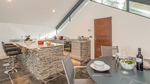 A modern kitchen with a stone island, a dining area with a table and chairs, and a large window providing natural light. - Boathouse on the Lake (Windermere)