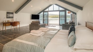 A spacious bedroom with a large bed, a desk, and a TV. - Boathouse on the Lake (Windermere)