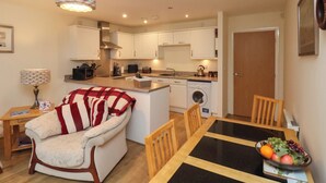 A compact living space with a kitchenette, a dining area with a table and chairs, a sofa, and a washing machine. - Cadliam (Whitby)
