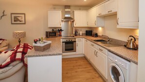A compact kitchen with white cabinets, a microwave, a toaster, a kettle, and a washing machine. - Cadliam (Whitby)