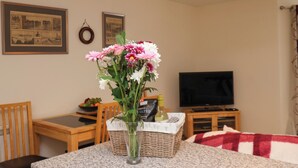 A dining area with a table, chairs, a vase of flowers, a basket with kitchen items, and a television on a stand. - Cadliam (Whitby)