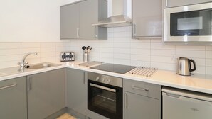 A modern kitchen with grey cabinets, a stainless steel microwave, a built-in oven, a kettle, and a toaster. - Samphire (Teignmouth)