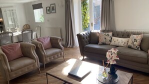 A living room with a sofa, two armchairs, a coffee table, and a dining area with a table and chairs. - The Granary (Bedford)
