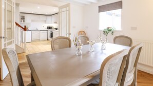 A modern kitchen with white cabinets, a dining area with a table set for four, and a view of the adjacent living space. - The Granary (Bedford)