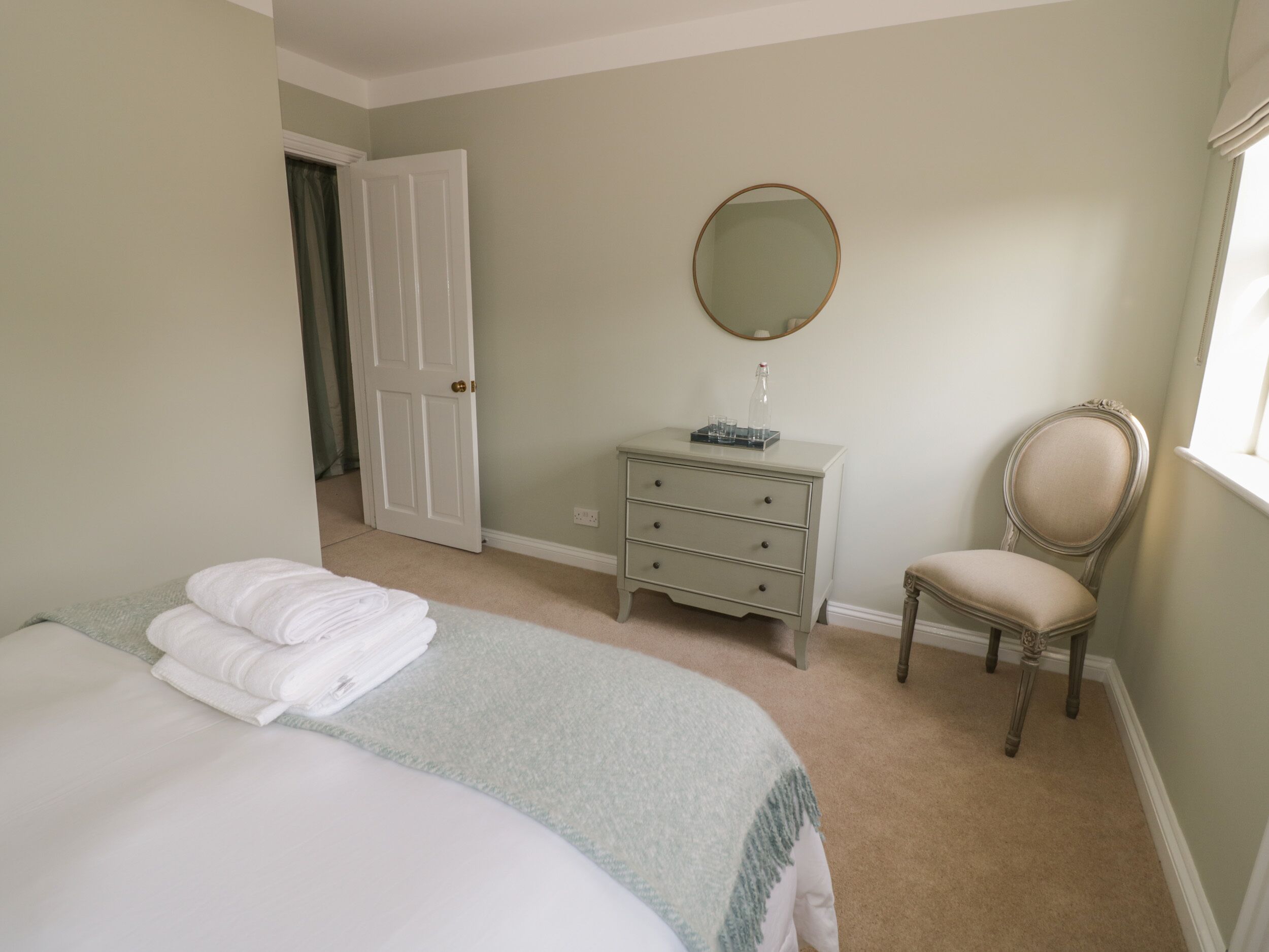 A bedroom with a bed, a dresser, a chair, and a mirror.