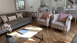 A living room with a grey sofa, two armchairs, a coffee table, and a dining area with a table and chairs. - The Granary (Bedford)