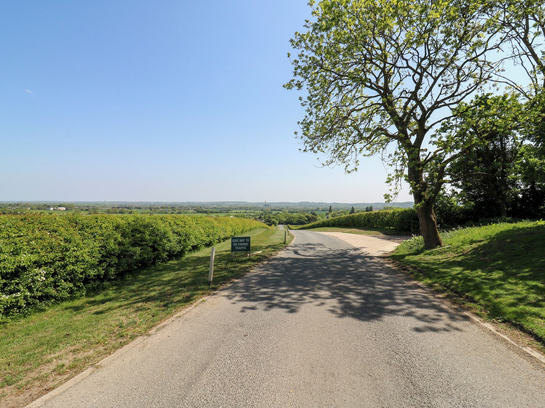 A rural road with a sign indicating 'Give Way to Oncoming Traffic'.