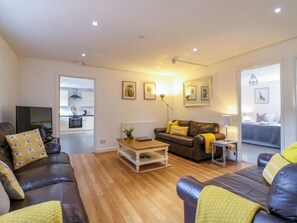 A living room with a sofa, a coffee table, and a television. There is a kitchen in the background. - BB House (Bedford)